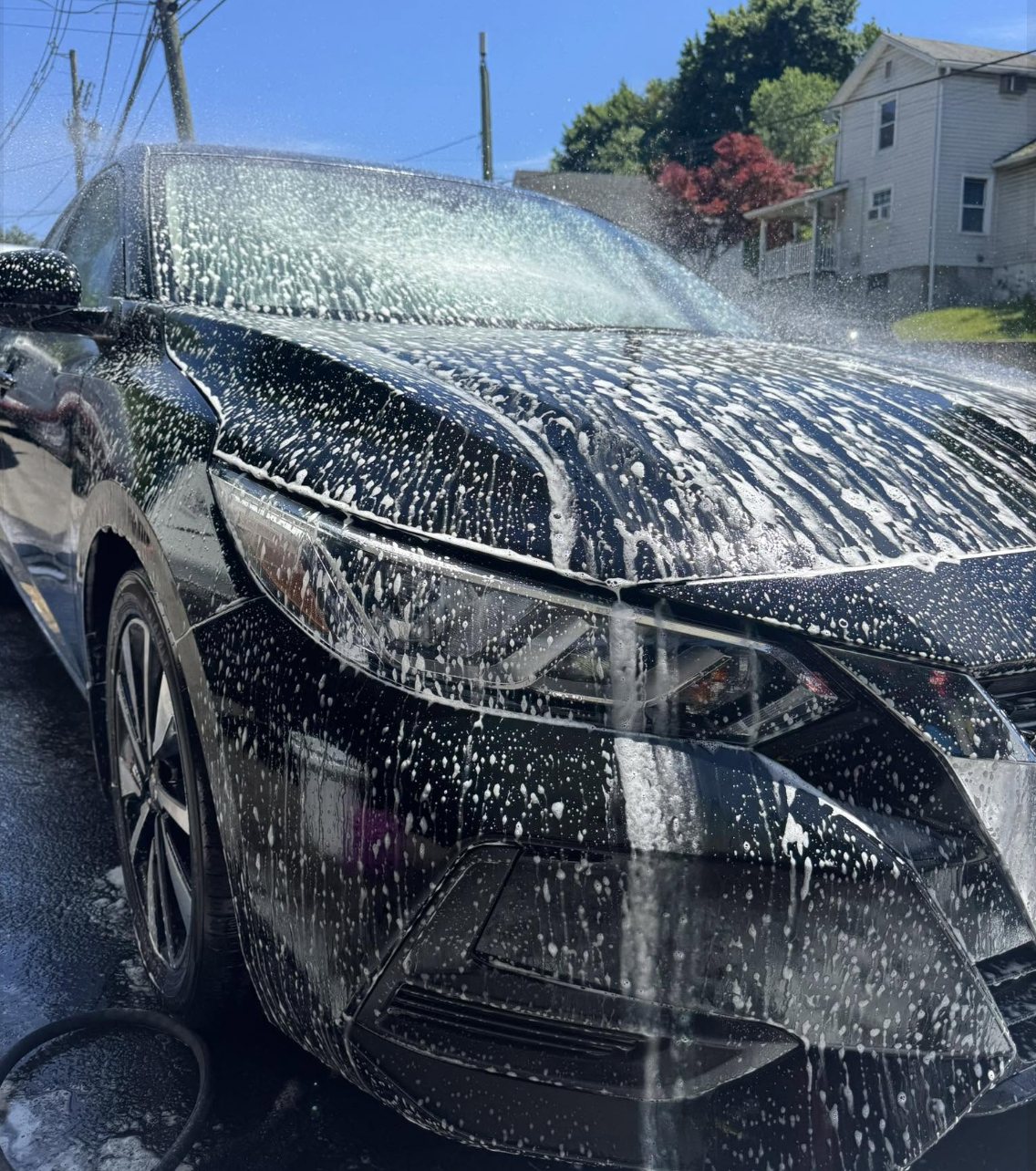 Foam bath being hand-applied to a black car exterior