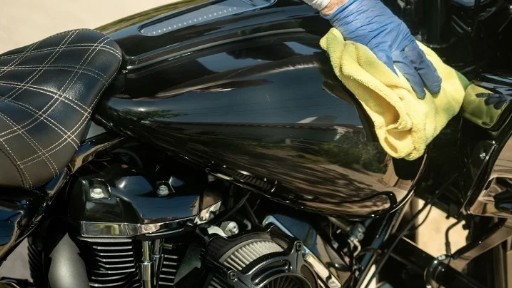 Hand-detailing a glossy black motorcycle gas tank with a microfiber cloth